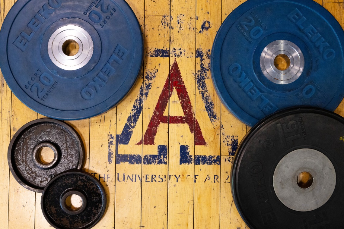 A faded UArizona Block A on the floor surrounded by different sizes of weights