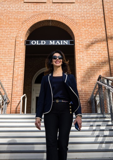 A photograph of a woman wearing sunglasses and smiling while walking down the steps of Old Main 