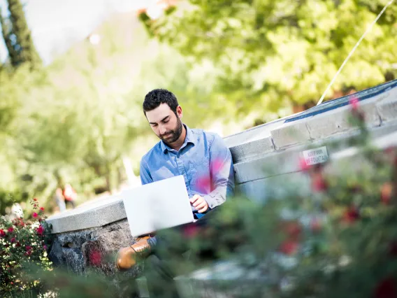 Man looking at laptop, sitting at Old Main Fountain