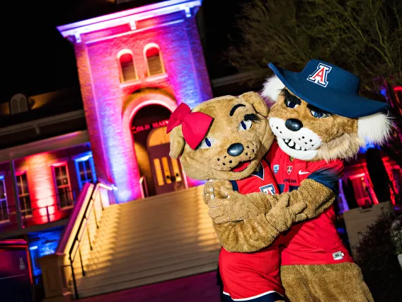 Wilbur and Wilma Wildcat mascots hugging in front of Old Main