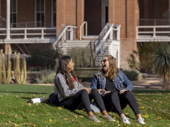 Two female students sitting on the grass in front of Old Main