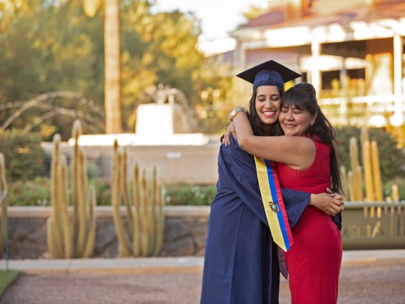 Woman in graduation cap and gown hugging her mother