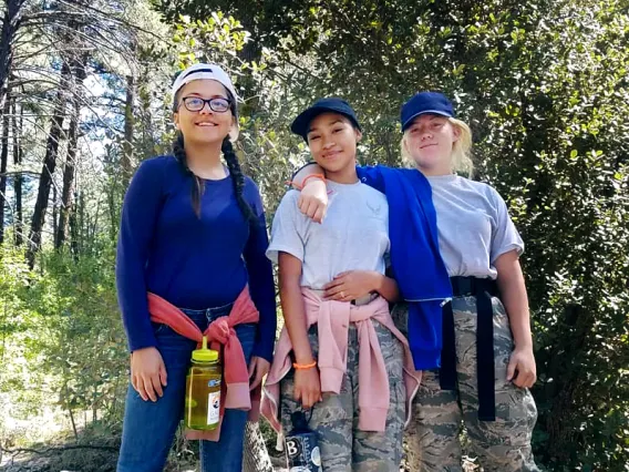 Three girls standing on log in the woods