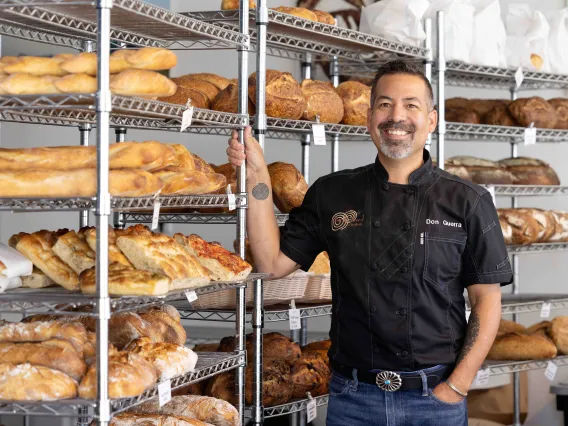 A man poses next to racks of freshly baked bread