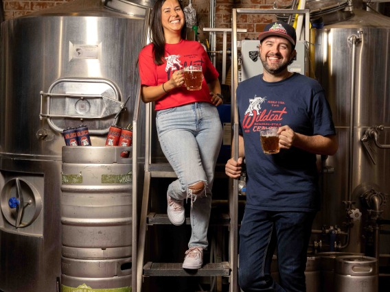 A woman and man pose near brewery equipment