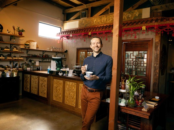 A man stands in a tea house environment holding a gaiwan