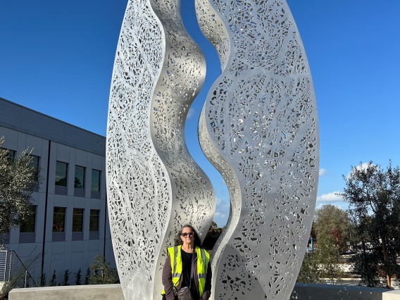Artist poses before a large-scale sculptural artwork with a bright blue sky