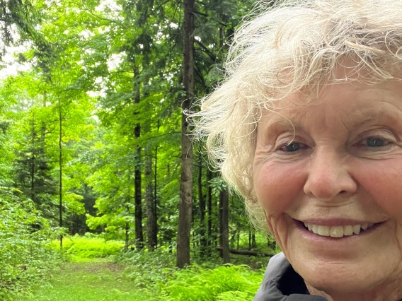 Woman smiles against a green forest backdrop in a selfie style portrait
