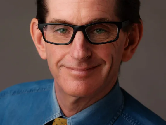 Professional headshot of man in dark rimmed glasses wearing business attire