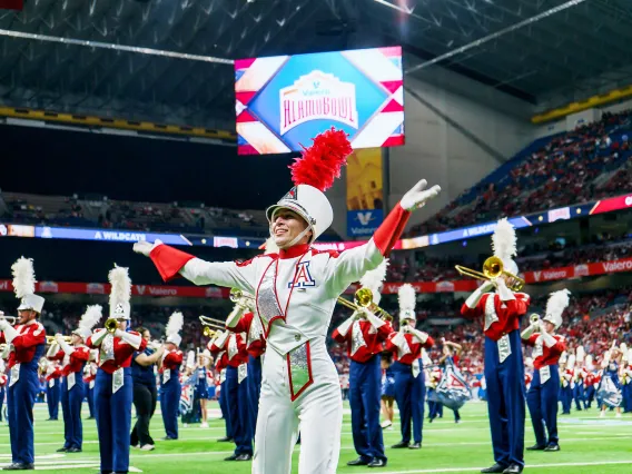 A member of the pride of Arizona marching band standing with their arms wide smiling with the band playing in the background