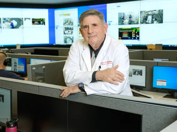 A photograph of a man smiling with his arms crossed over a desk 