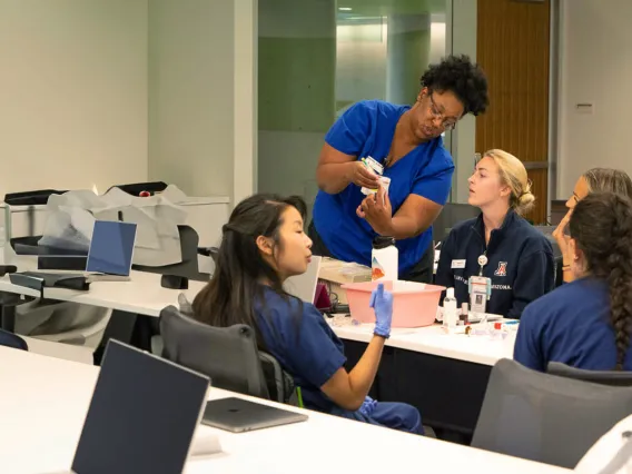 A photograph of an instructor teaching a group of five nurses, sitting around a table 