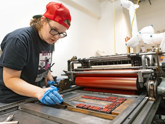 Image of Cameron Kramer using a Vandercook proving machine to work on their final project.