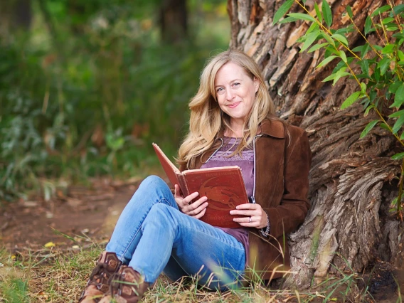 Laura smiling, holding a book under a tree