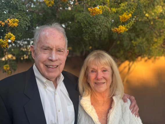 Don, who is wearing a suit, is smiling, with his arm around Susan, who is wearing a white sweater