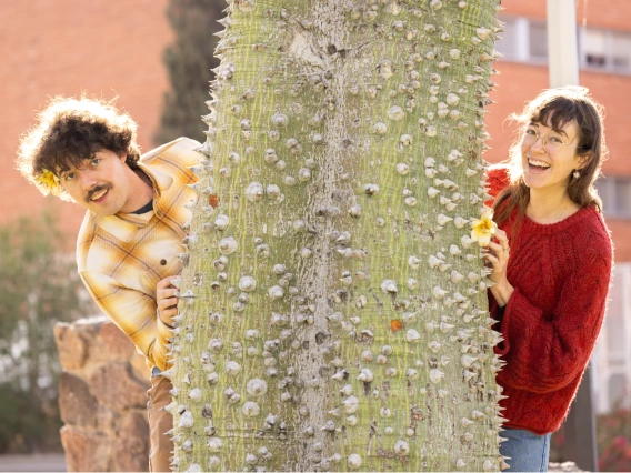 A couple peeking at both sides of a tree 