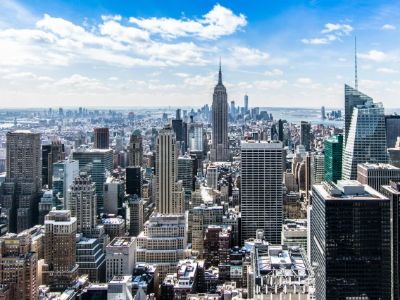 A photo of the New York City skyline during the daytime. It is a bright, beautiful day with some clouds in the sky.