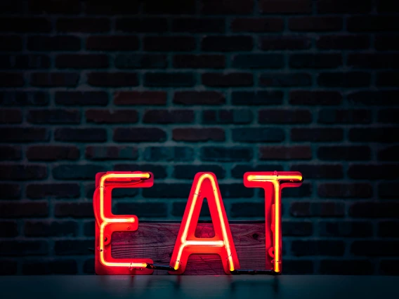 Image of a neon orange sign that says EAT in all capital letters aganist a black background.