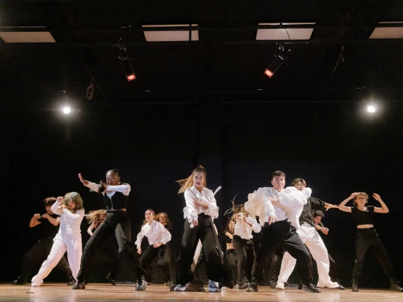 Large dance group in coordinated black and white outfits performs a powerful routine in perfect formation on stage.