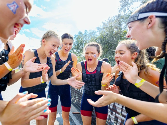 Arizona triathlon athletes form a huddle, cheering and clapping in celebration after a race.