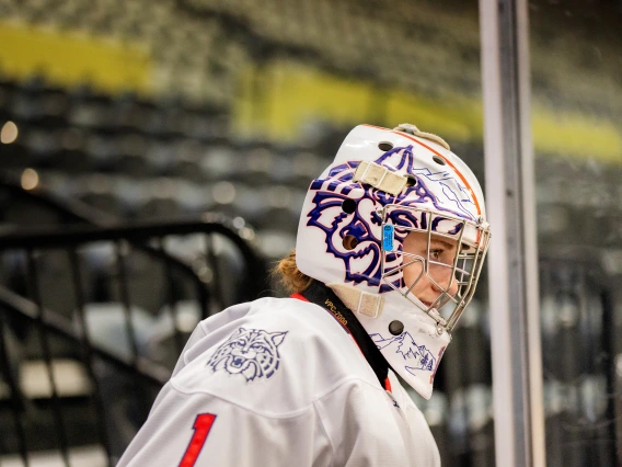 Arizona goalie in a custom-designed Wildcat helmet stands alert near the boards, watching the game.