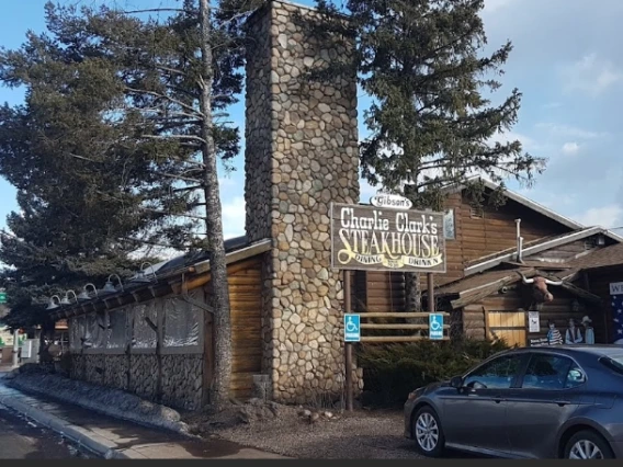 A log cabin with a stone chimney with the words "Gibson's Charlie Clark's Steakhouse Dining Drink'n" 