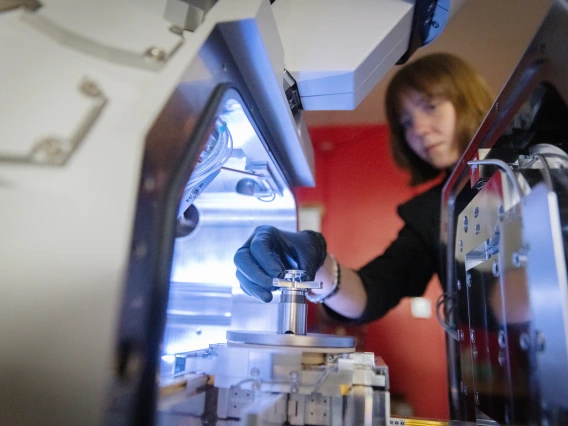 A researcher examines asteroid sample particles in a laboratory, with precision instruments and sterile handling tools visible.