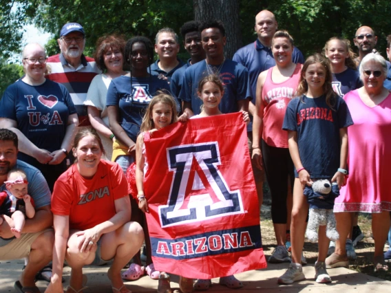 A group of people from all ages smiling and wearing U of A clothing