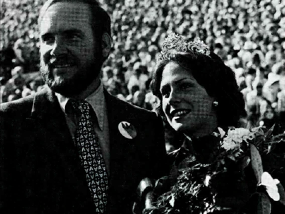 A homecoming king and homecoming queen smiling on a football field