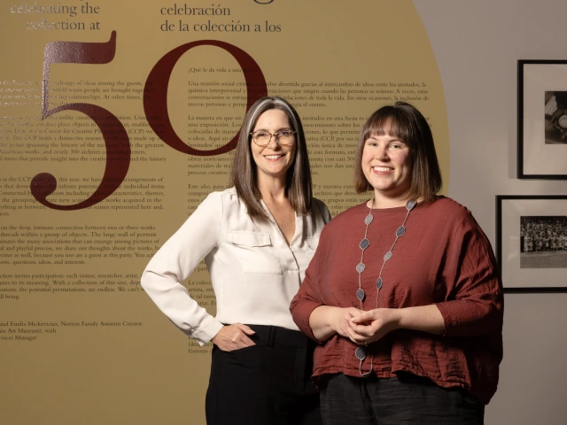 Rebecca Senf and Emilia Mickevicius smiling in front of a wall with a giant red 50 painted on it.