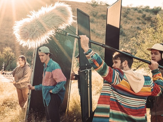 a group of people standing in a grassy valley at golden hour with a boom mic and other filming equipment