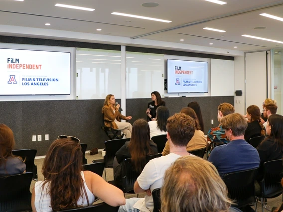 A group of University of Arizona alumni and guests sit in a modern conference room listening to a panel discussion hosted by Film Independent and the University of Arizona’s Film & Television Los Angeles program. Two women are seated at the front speaking into microphones, with dual screens behind them displaying the Film Independent and UArizona FTV LA logos.