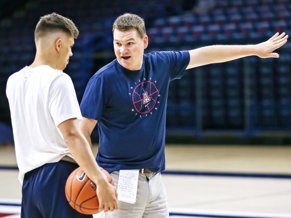 A photograph of Tommy Lloyd, the current University of Arizona basketball coach, speaking with a basketball player.