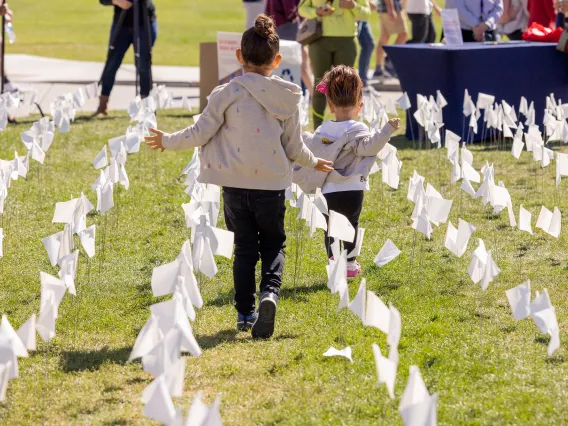 A photograph of two young girls running through a green field with white flags.