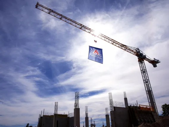 A photograph of a crane holding the University of Arizona Block 'A' Flag against a cloudy backdrop.