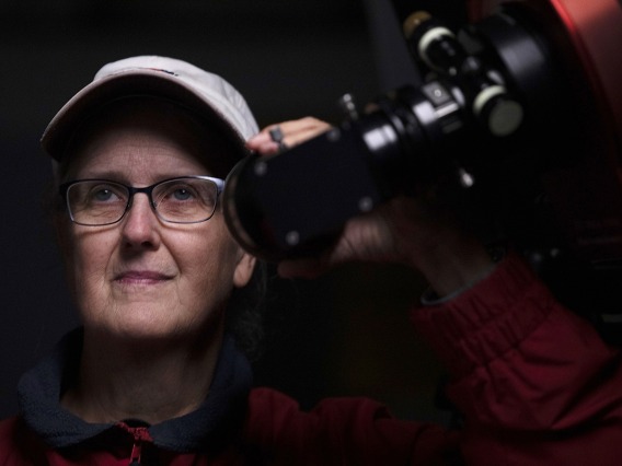 A photograph of Marcia Rieke, the Regents' Professor of Astronomy and associate department head at the University of Arizona, looking through a telescope lens.