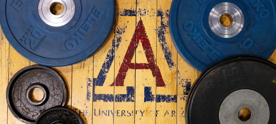 A faded UArizona Block A on the floor surrounded by different sizes of weights