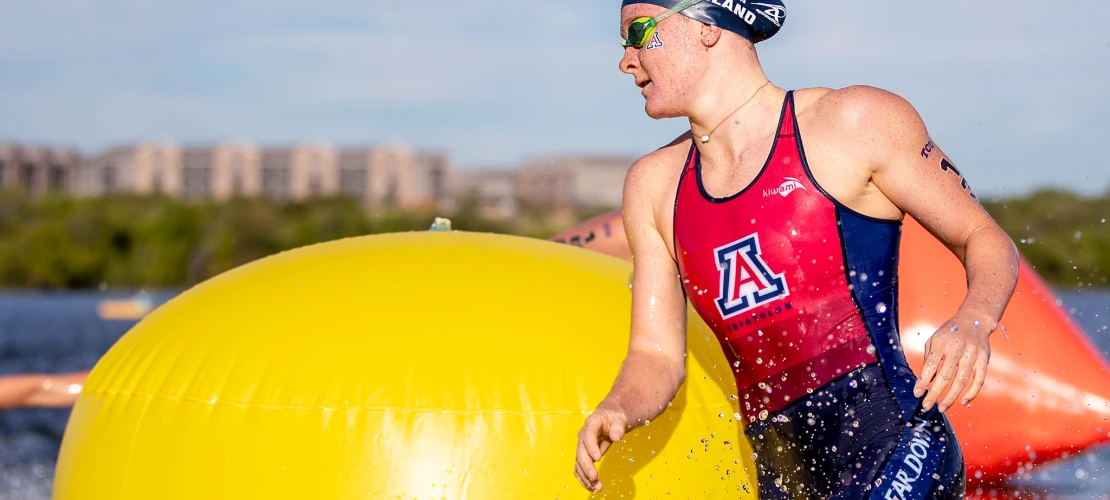 Arizona triathlete exits the water during the swim portion of a race, passing a bright yellow buoy and wearing a swim cap and goggles.
