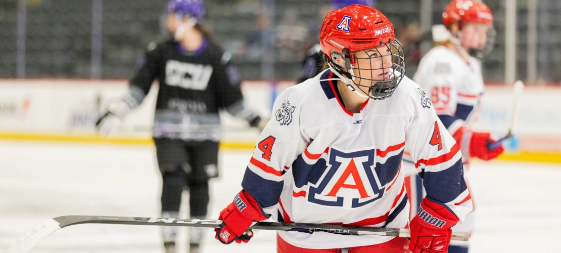Arizona player in a white and red jersey with number 4 skates across the ice, focused during gameplay.