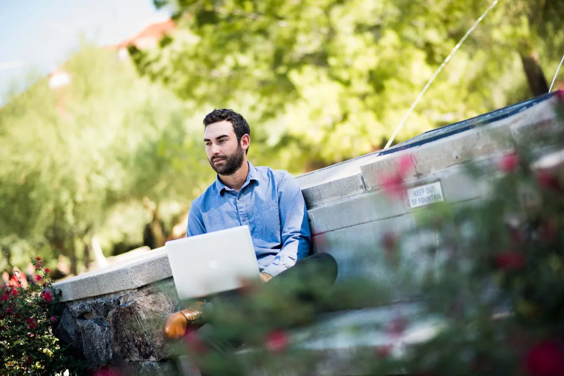 Person working on laptop in front of a fountain. 