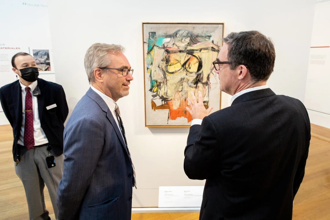 Two men talking in front of painting