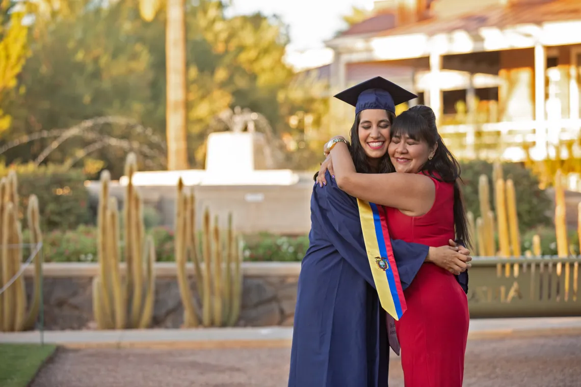 Woman in graduation cap and gown hugging her mother