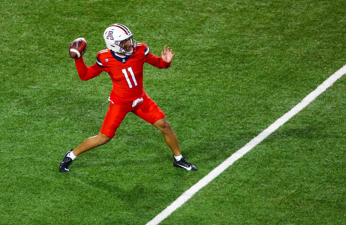 A football player in red throws a ball on a green field