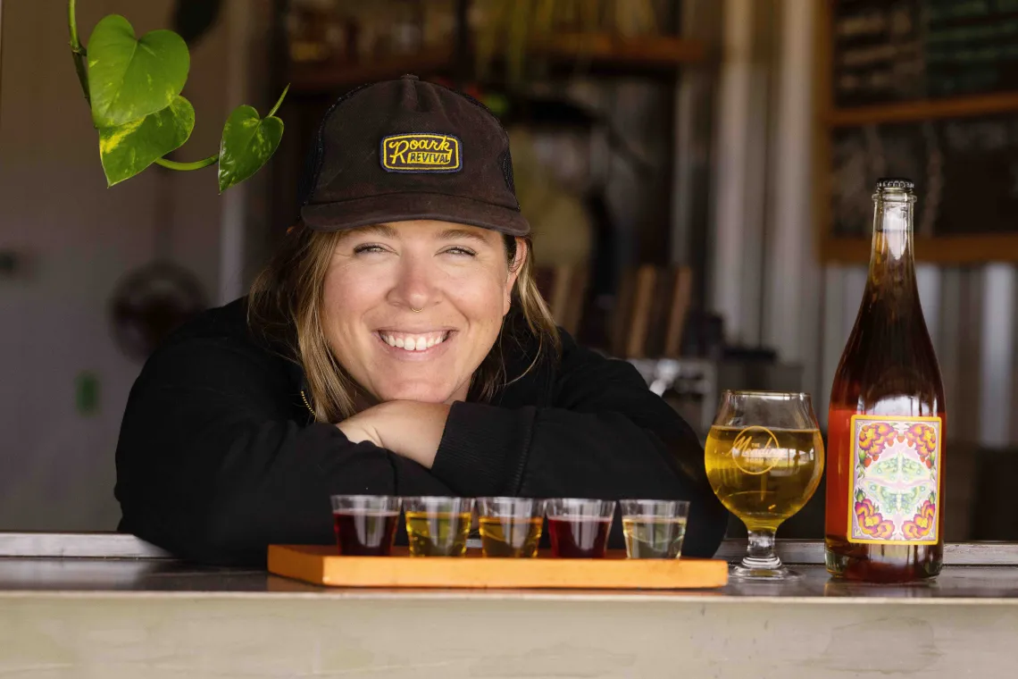 Woman smiles posing next to flight of mead samples