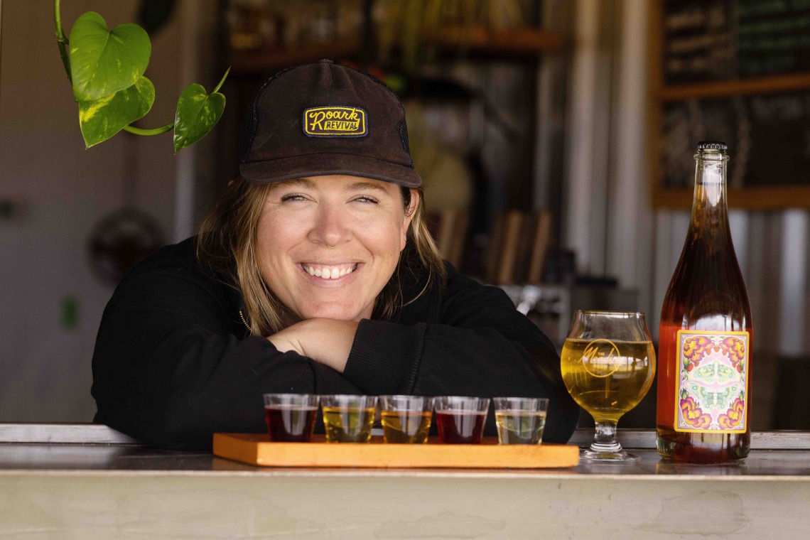 Woman smiles posing next to flight of mead samples