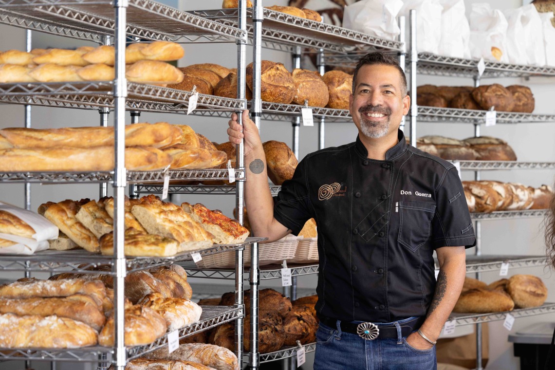 A man poses next to racks of freshly baked bread