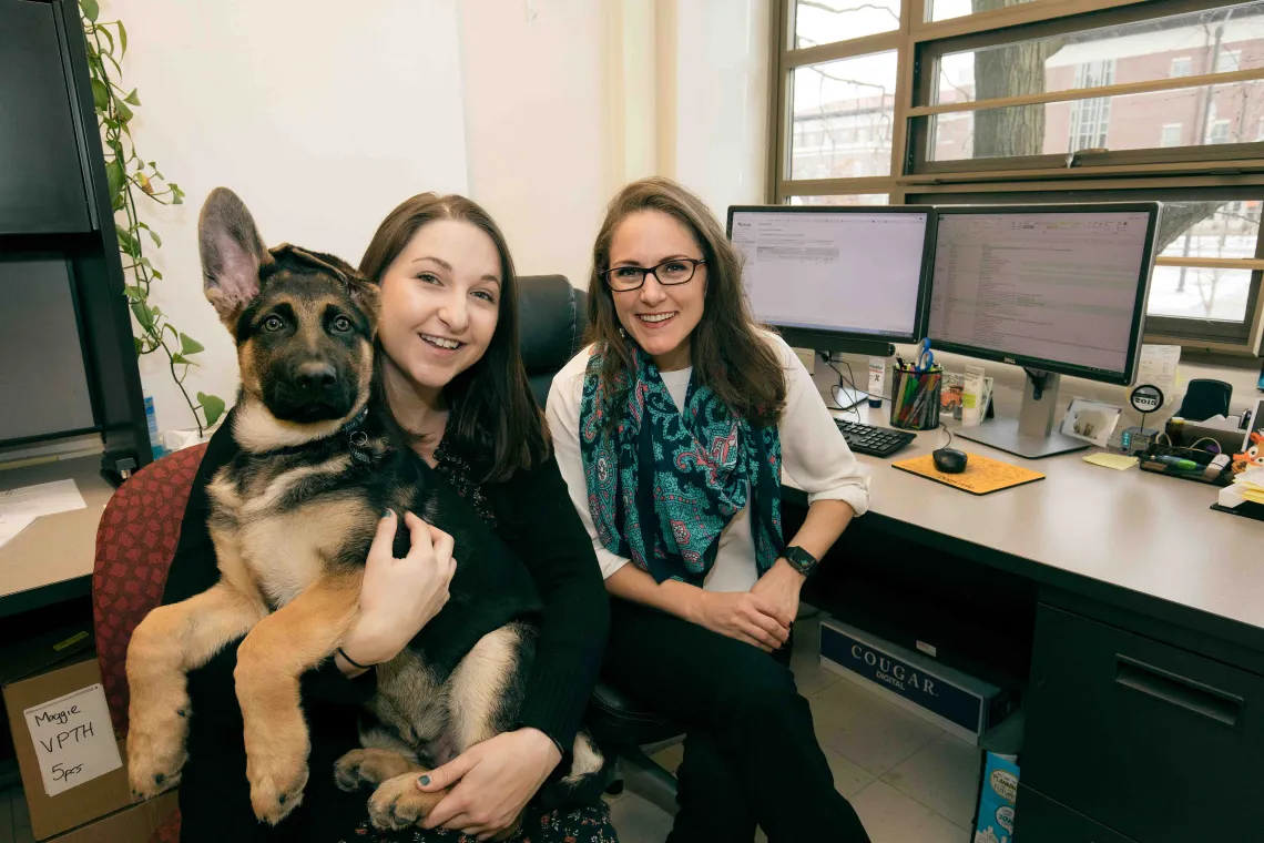 Two researchers pose with Hendrix the German shepherd.