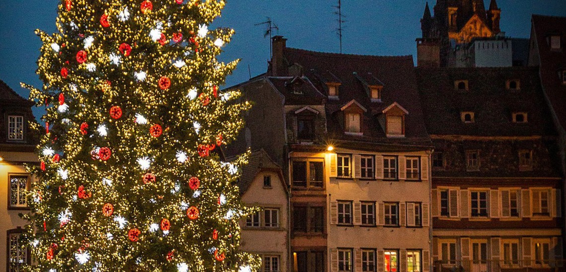 A town center at dusk with a bright holiday tree at the front