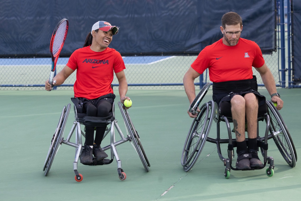 A photograph of one man in a wheelchair smiling and another man in a wheelchair focused with his eyes down