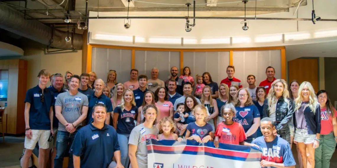 Alumni, students and their families smiling while holding a UArizona banner